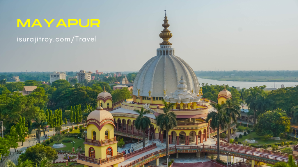 Capture the serenity of Mayapur, West Bengal, India. A tranquil riverside view with majestic temples, lush greenery, and a spiritual atmosphere.
